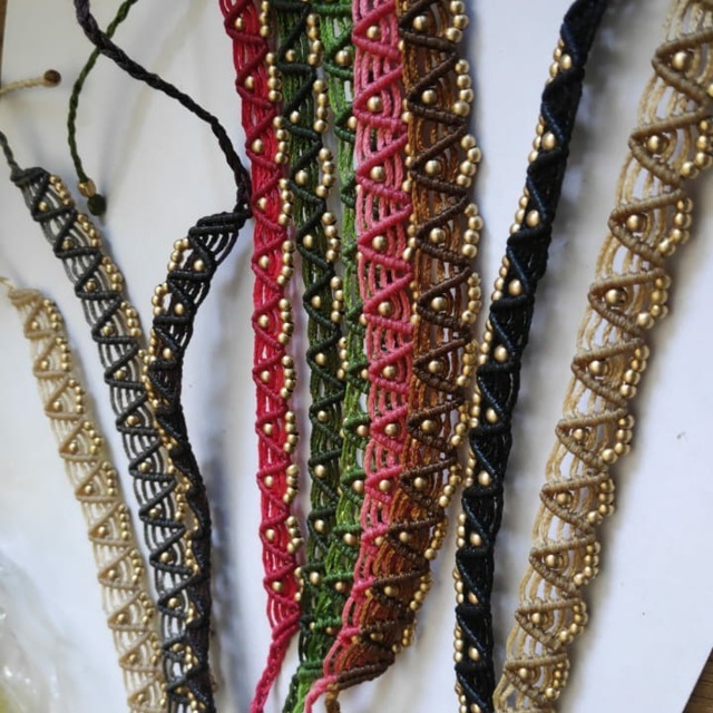 Ein Armband oder Fußkettchen aus Makramee mit bunten Fäden und Bronzeperlen.